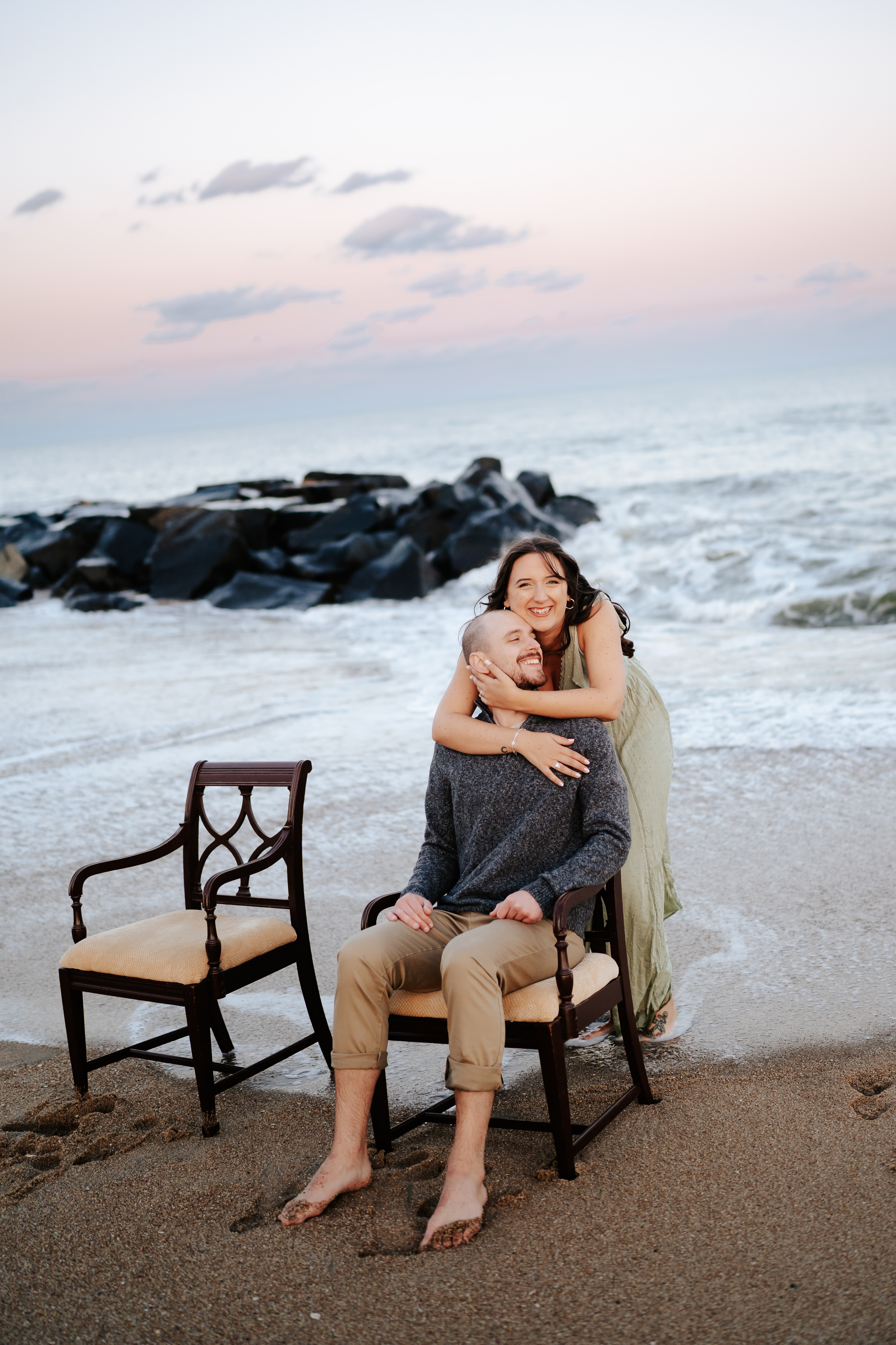 A couple holding hands on vintage chairs at Asbury Park Beach during their engagement session with Maryland Wedding Photographer capturing the serene ocean backdrop.