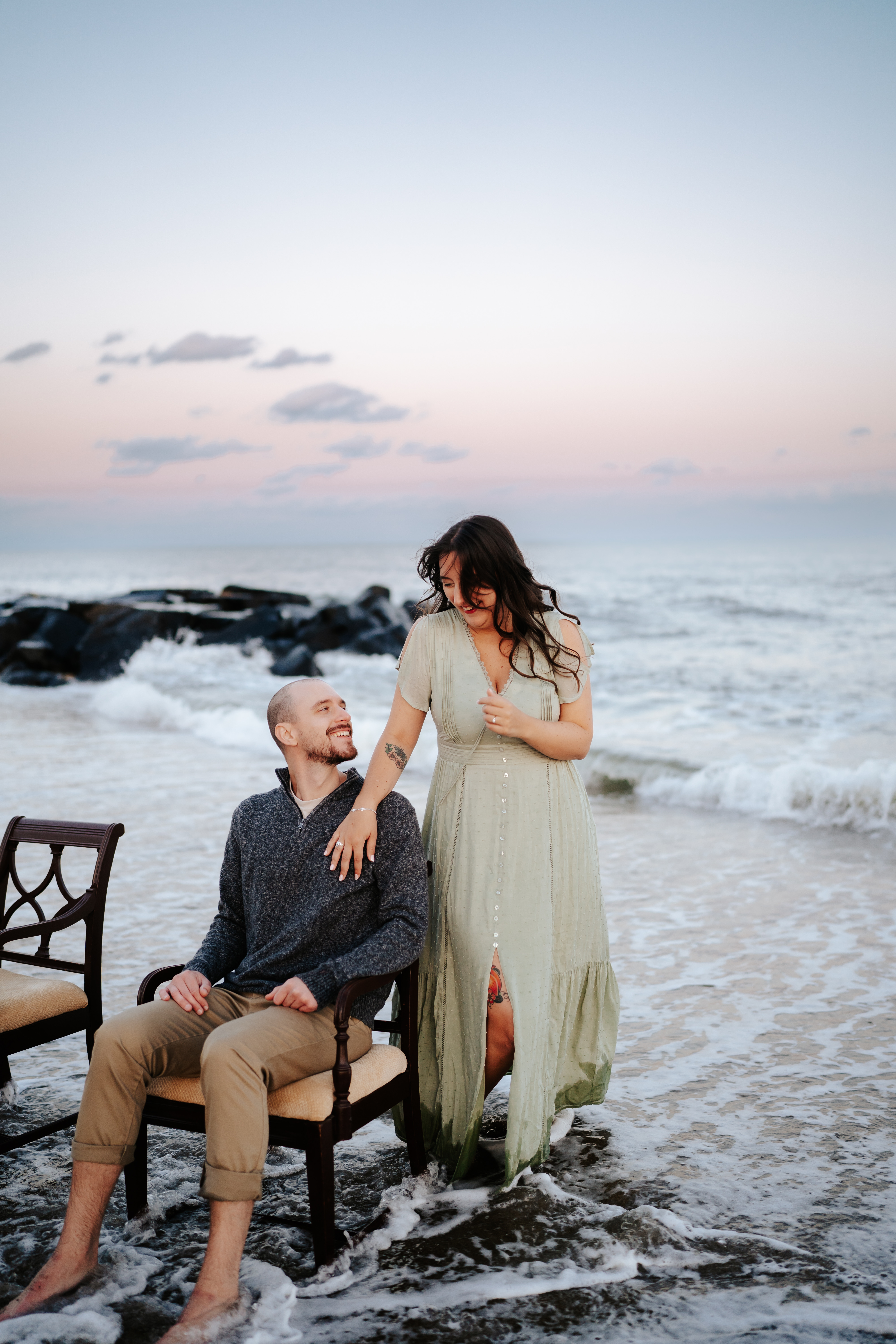 A couple holding hands on vintage chairs at Asbury Park Beach during their engagement session with Maryland Wedding Photographer capturing the serene ocean backdrop.