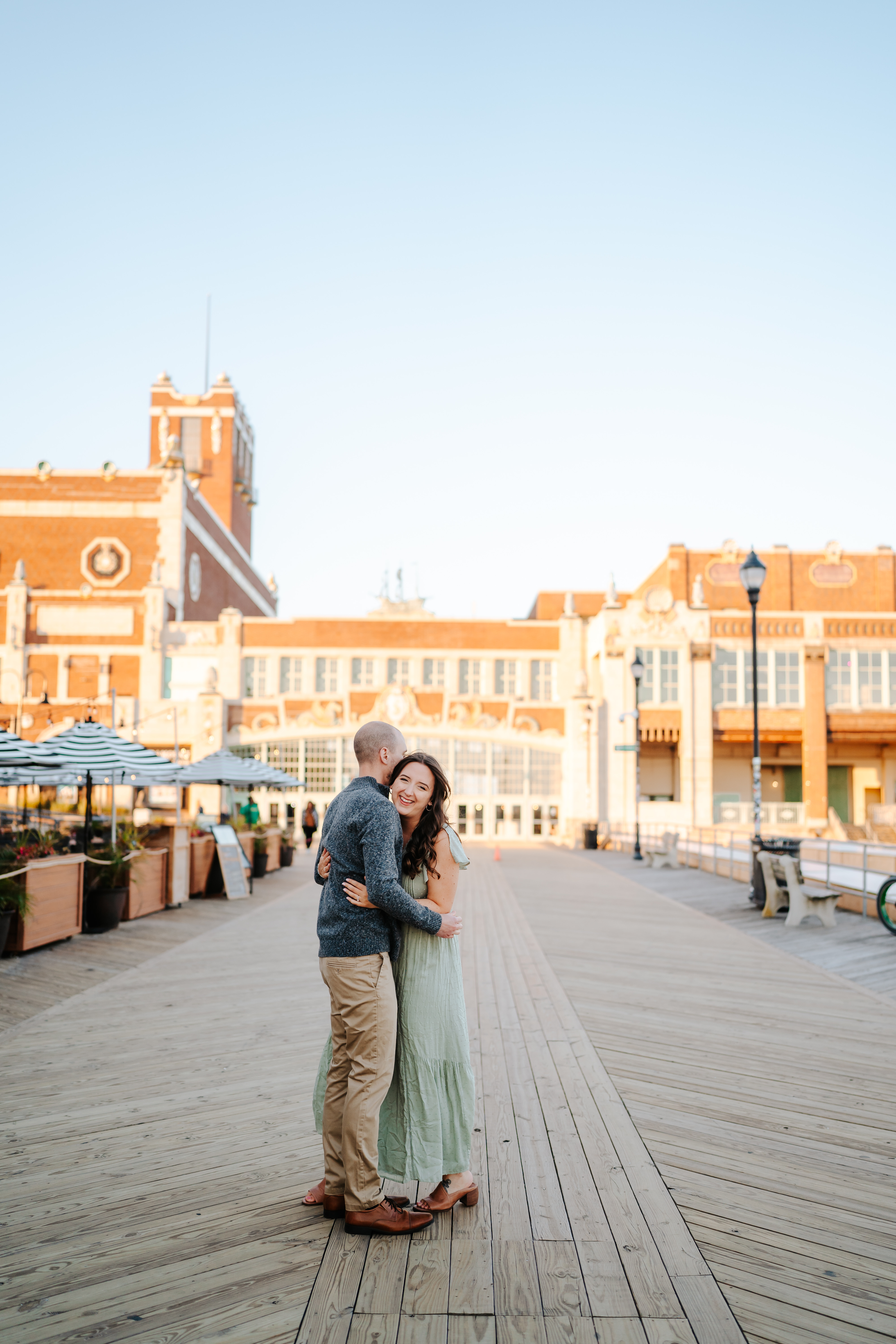 Couple embracing in a sun-kissed engagement photo on Asbury Park Boardwalk, captured by Maryland Wedding Photographer, showcasing candid love and joyful moments