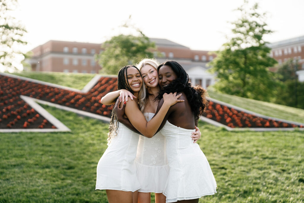 3 Best friends hugging and smiling as they celebrate their graduation in front of "The M" at the University of Maryland captured by Brenna Marie Photography