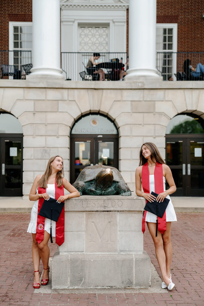 UMD Grads smiling next to Testudo wearing graduation stoles and holding their graduation caps. Spring Graduation Photography Session at The University of Maryland College Park, Maryland captured by UMD Graduation Photographer Brenna Marie Photography