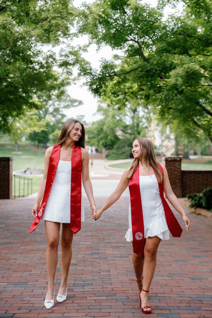 University of Maryland graduates holding hands and walking together on a brick path at McKeldin Mall laughing with each other