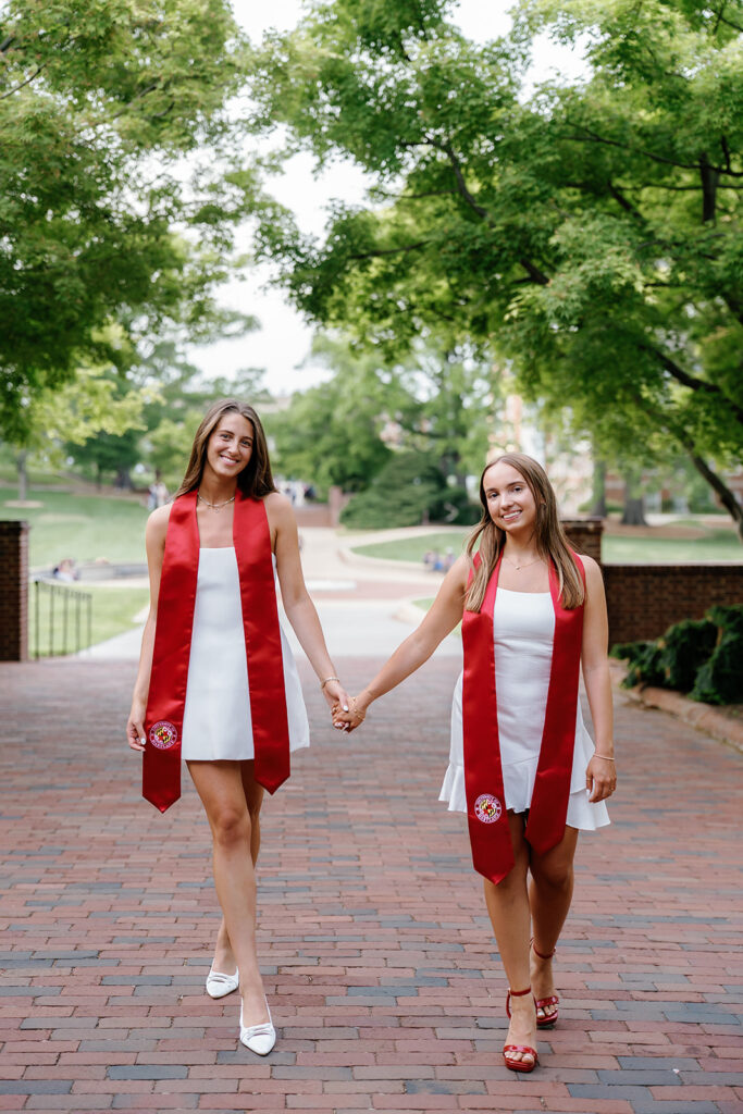 University of Maryland graduates holding hands and walking together on a brick path at McKeldin Mall