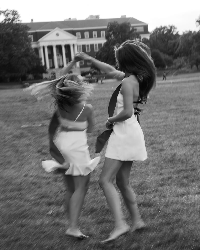Motion blur slow shutter speed image of 2 best friends running through a field wearing white dresses and their graduation stoles at The University of Maryland McKeldin Mall
