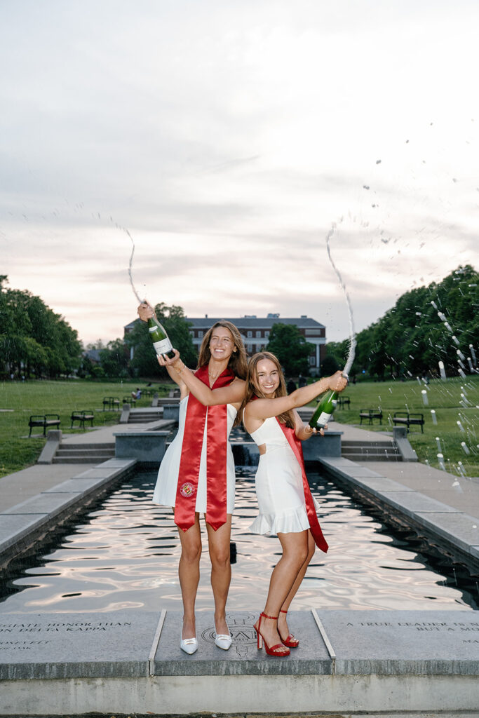 University of Maryland graduates standing on the fountain at McKeldin mall celebrating graduation with a champagne pop and spray
