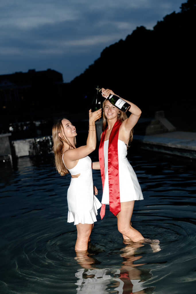 Flash photography of 2 University of Maryland graduates standing in the fountain at McKeldin mall cheersing champagne